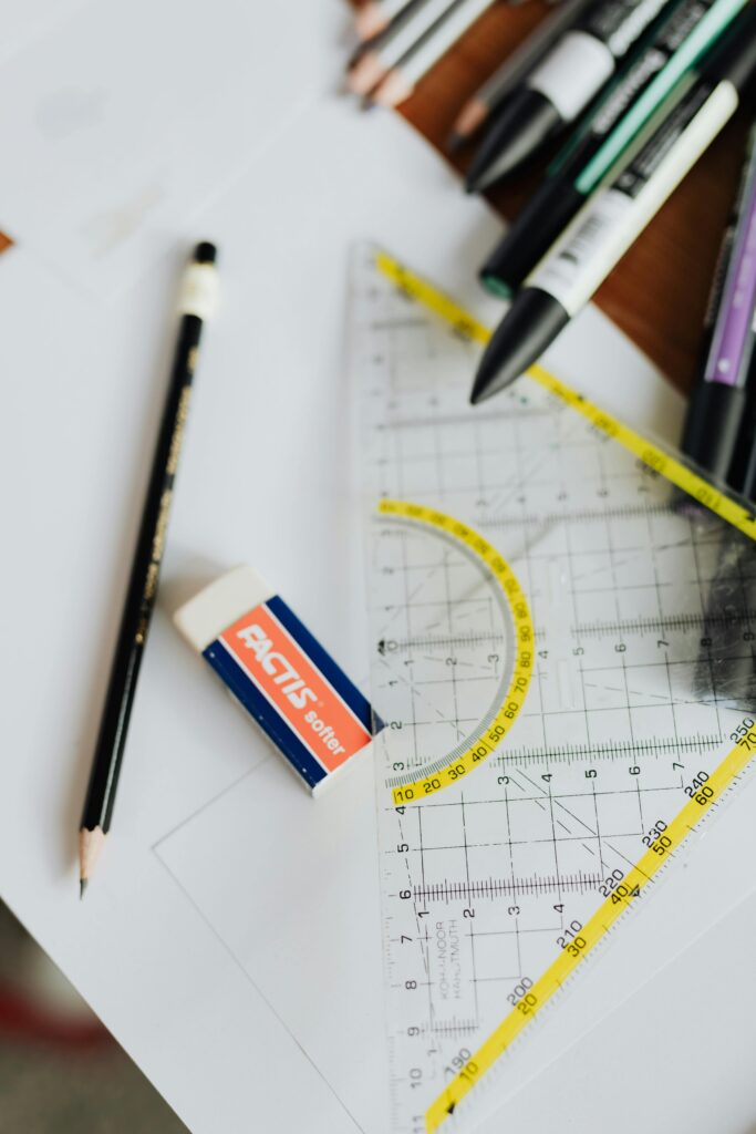From above of pencil with eraser on blank paper near drawing triangle with marked numbers and lines and kit of markers on table