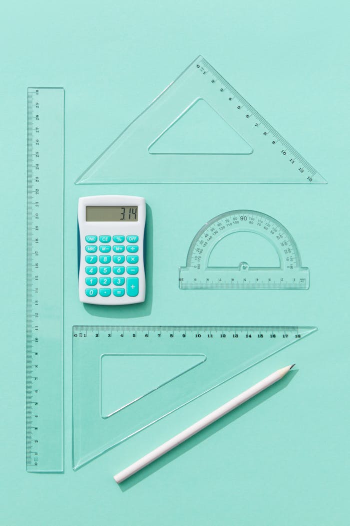Flat lay of calculator, rulers, and protractor on teal background, ideal for educational concepts.